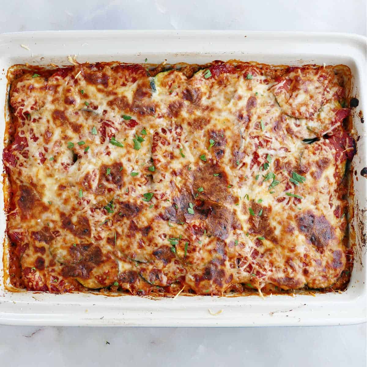 Baked zucchini ground beef casserole in a white baking dish.