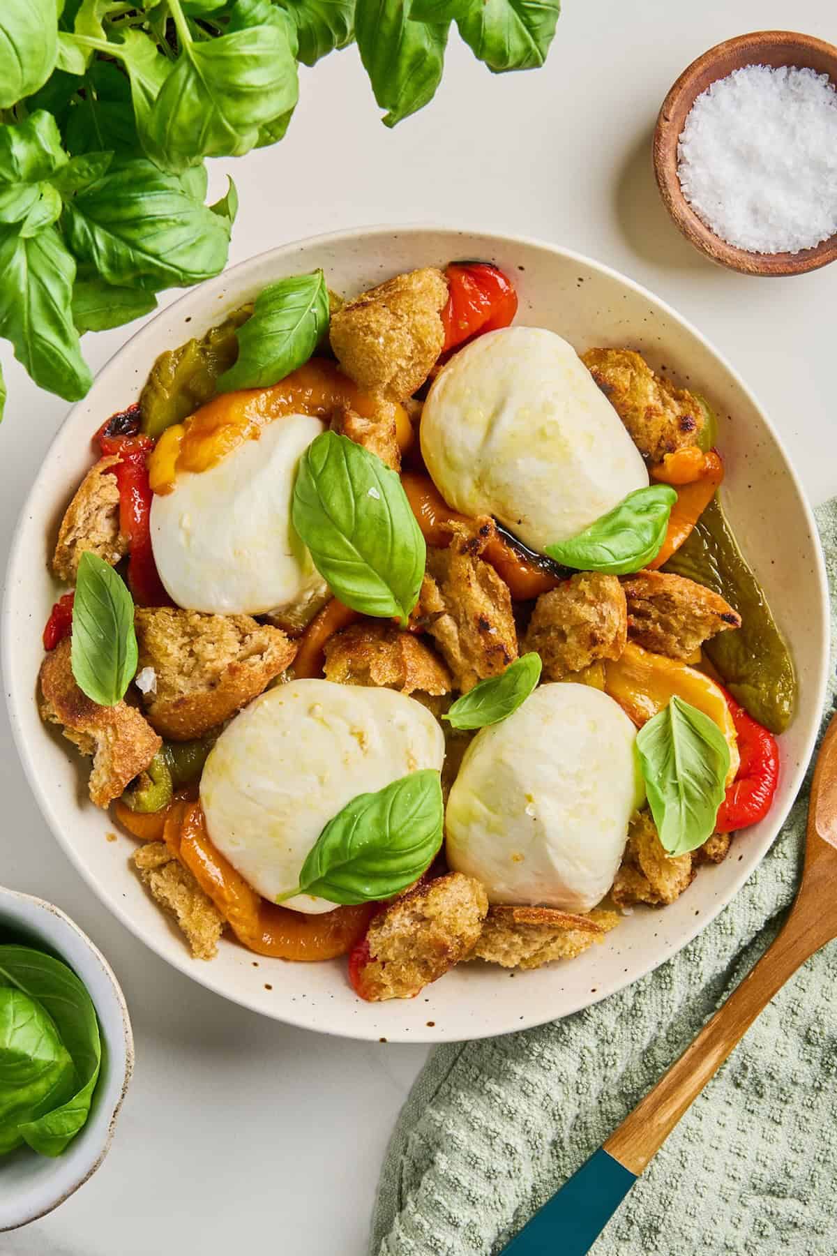 Roasted bell pepper salad with burrata and basil on a plate surrounded by ingredients.