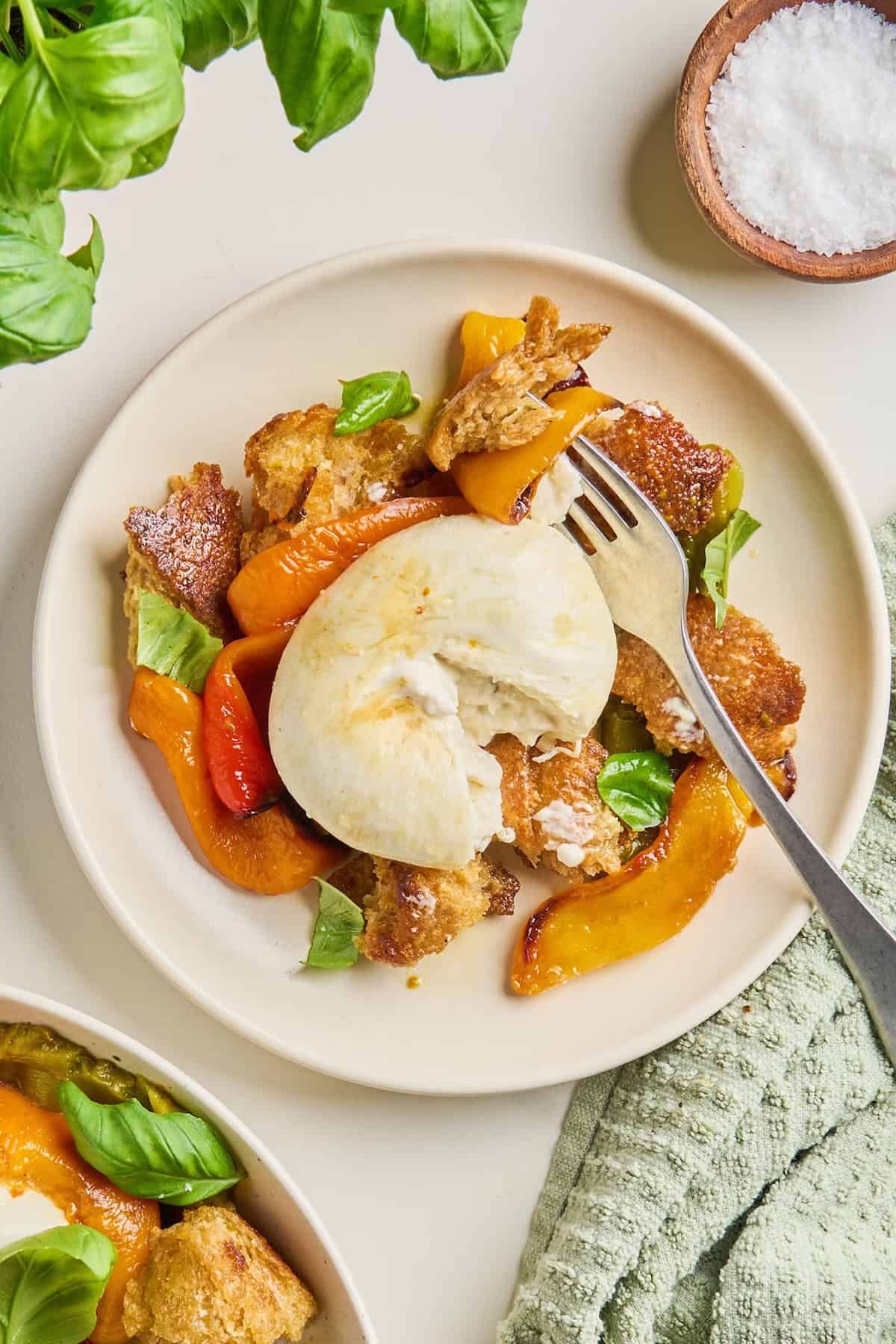 Bell pepper salad with burrata and a fork on a plate surrounded by napkin and garnishes.