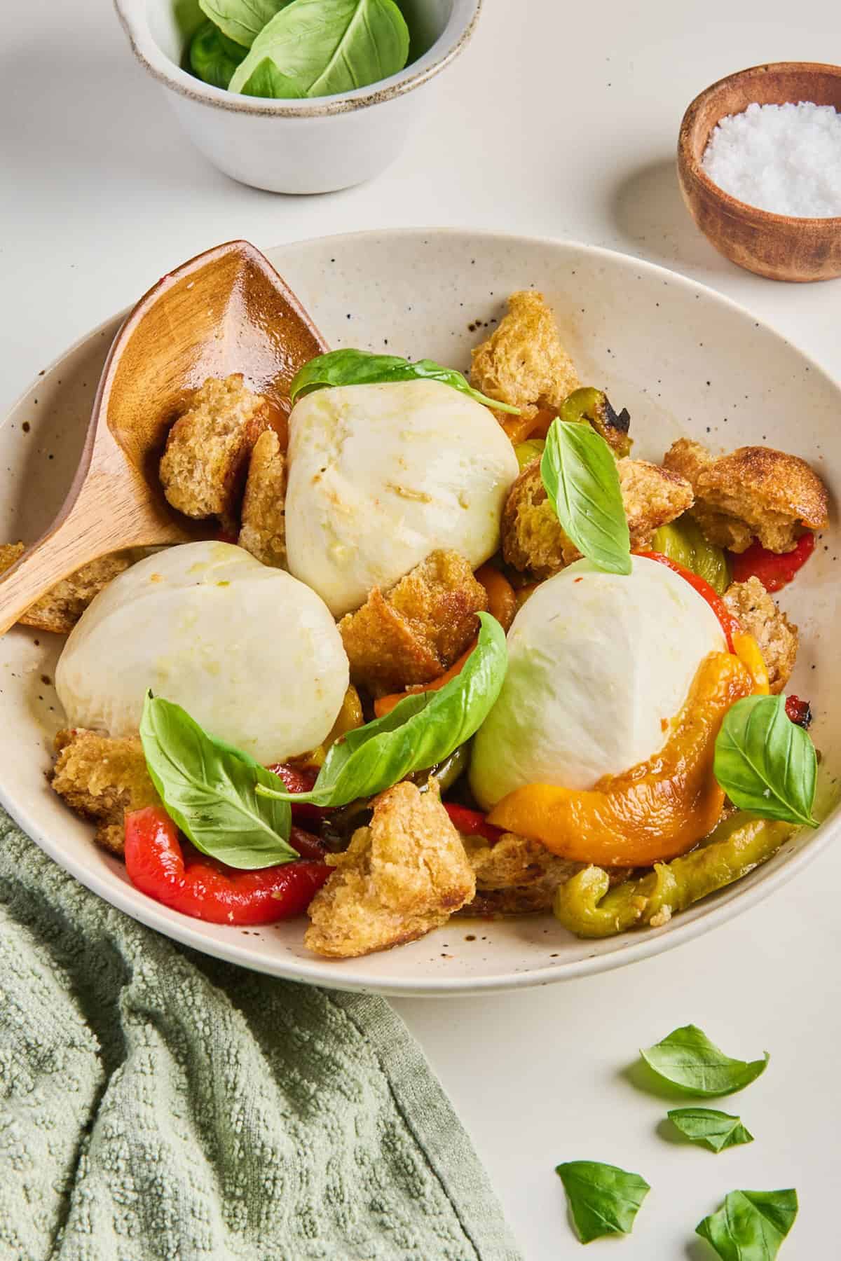 Bell pepper, burrata, and crouton salad in a bowl with a wooden spoon.