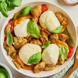Roasted bell pepper salad with burrata and basil on a plate surrounded by ingredients.
