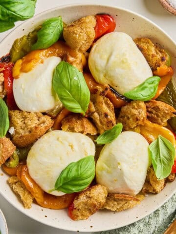 Roasted bell pepper salad with burrata and basil on a plate surrounded by ingredients.