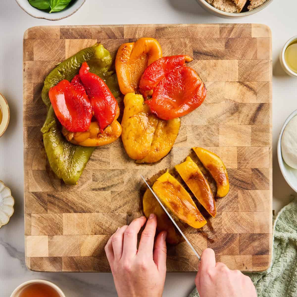 Woman slicing roasted yellow bell pepper into strips on a cutting board.