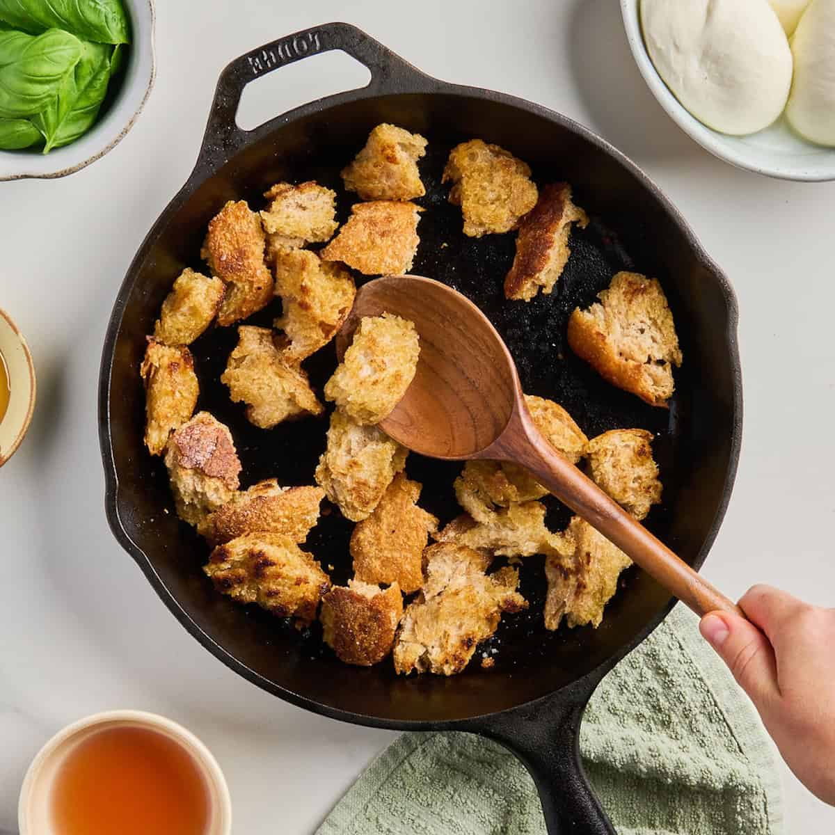Woman stirring torn sourdough bread cooking into croutons in a cast iron skillet.
