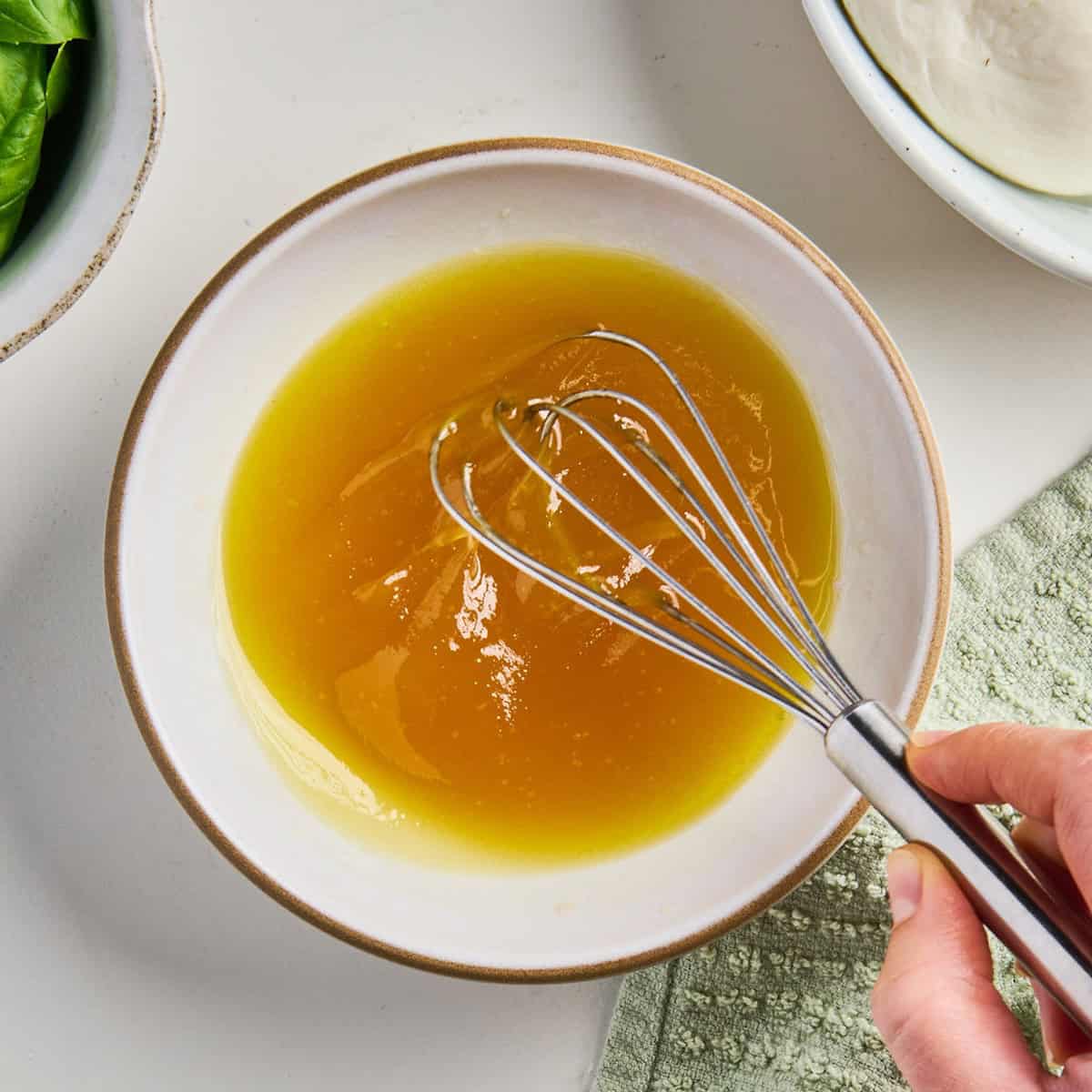 Woman whisking olive oil, red wine vinegar, and honey in a bowl.