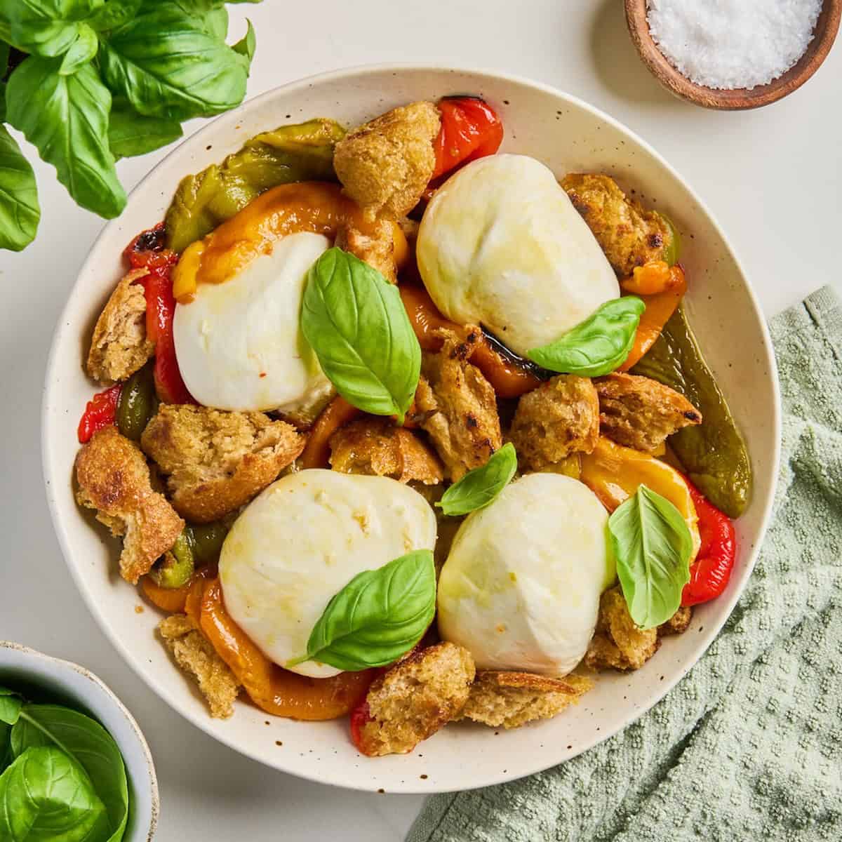 Roasted bell peppers, burrata cheese balls, and fresh basil arranged on a plate.