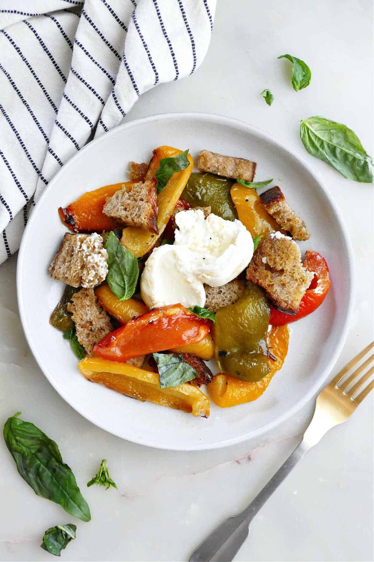 Serving of roasted bell pepper salad on a plate next to a fork and napkin.