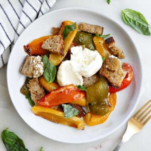 Serving of roasted bell pepper salad on a plate next to a fork and napkin.