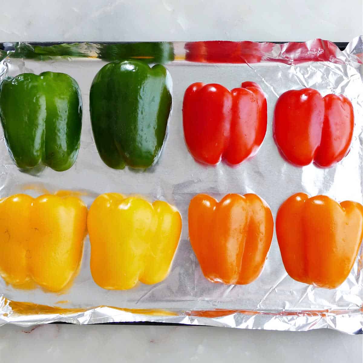 Colorful bell peppers prepared for roasting on a baking sheet.