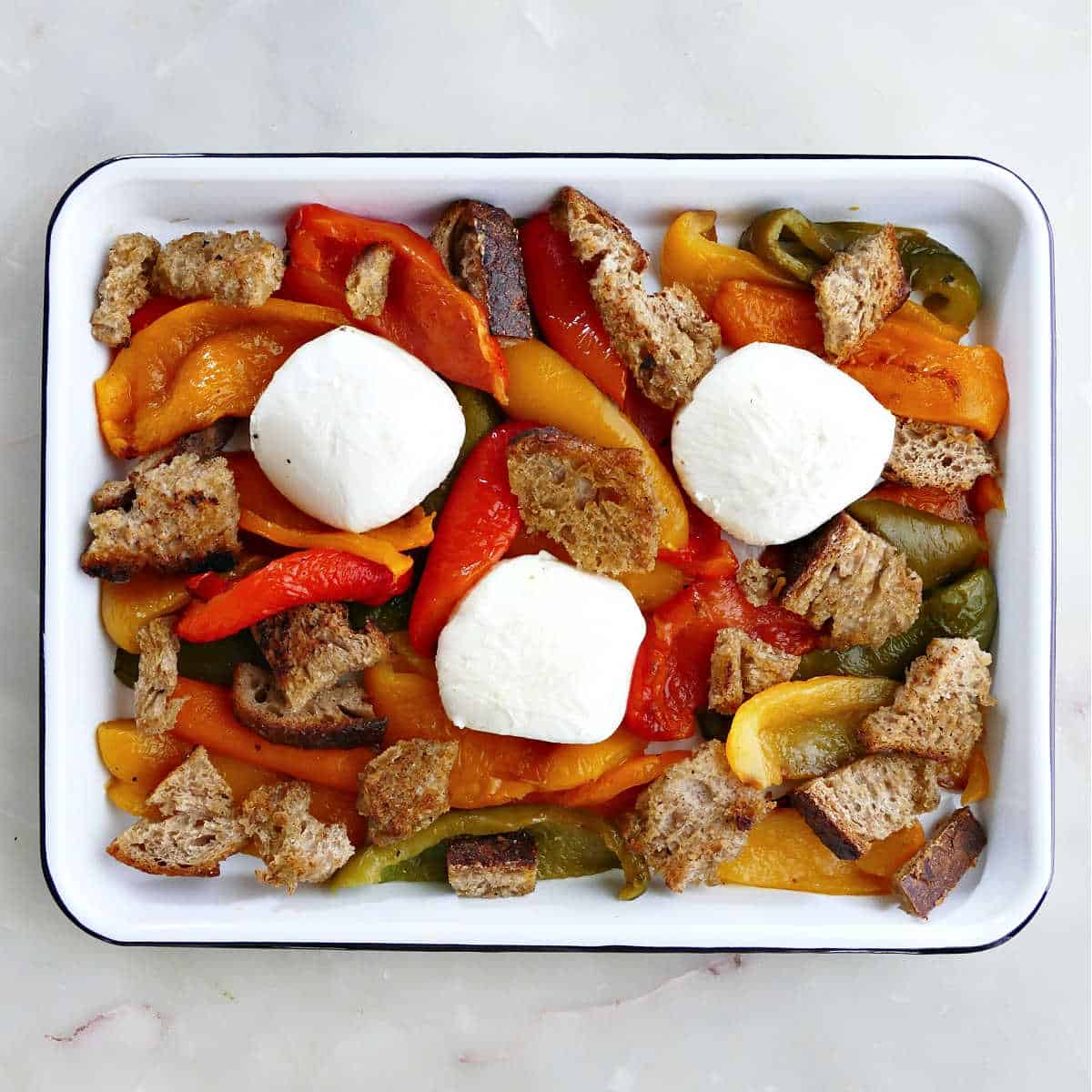 Roasted peppers, burrata balls, and croutons on a dish before garnishing.