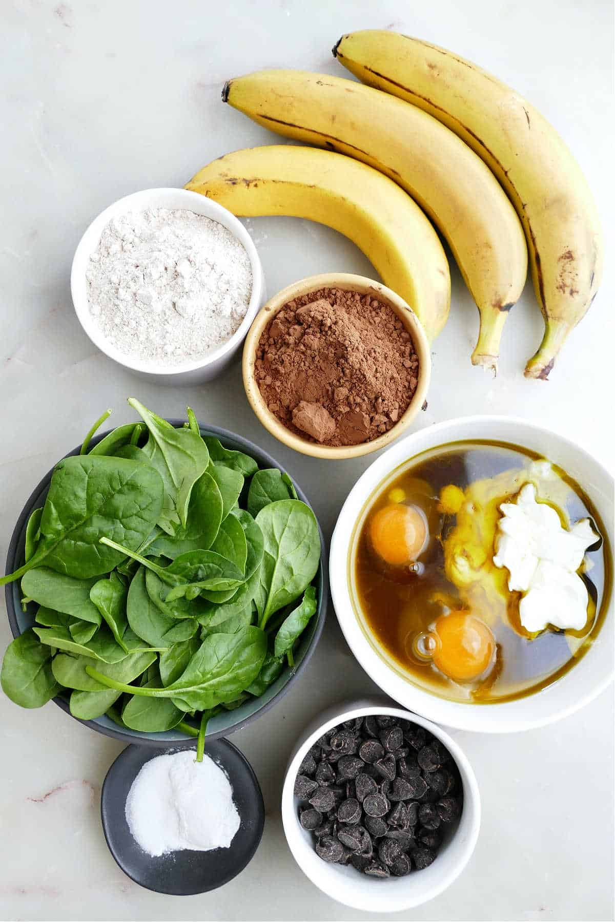 Bananas, flour, cocoa powder, spinach, chocolate chips, and wet ingredients for muffins.