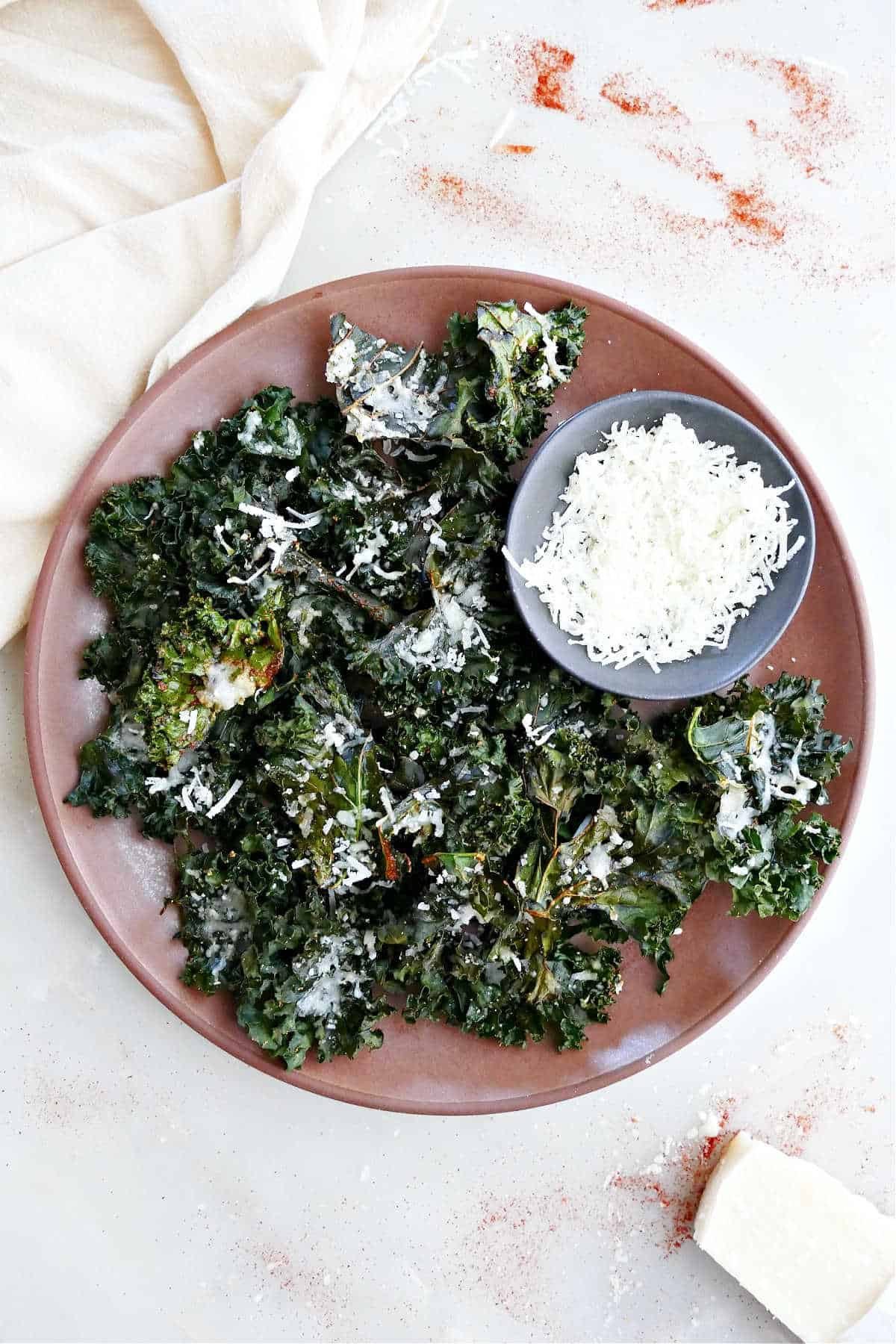 Crispy parmesan kale chips on a platter with a bowl of cheese.