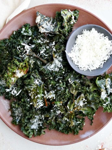 Crispy parmesan kale chips on a platter with a bowl of cheese.