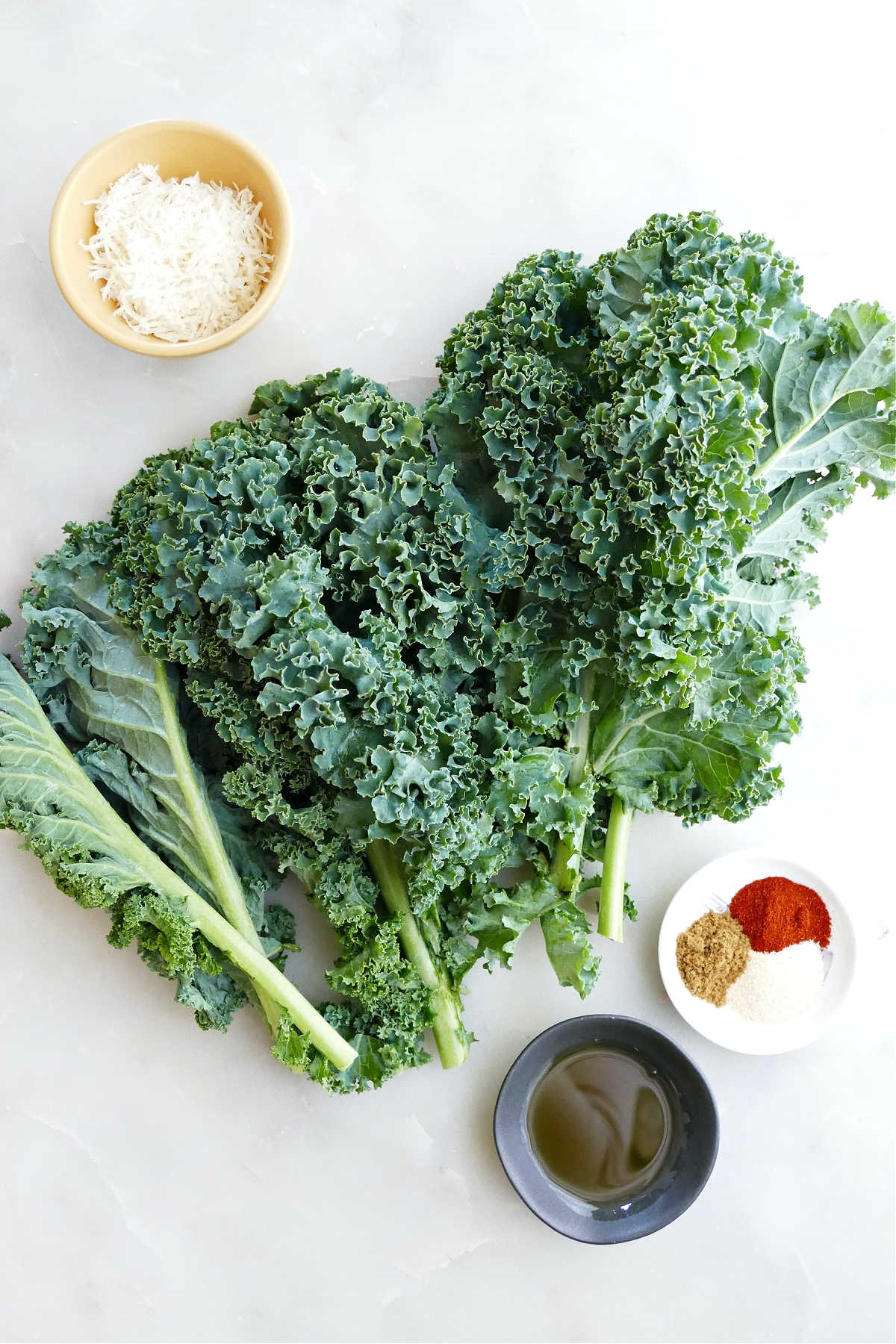 A bunch of curly kale, parmesan cheese, oil, and spices on a counter.