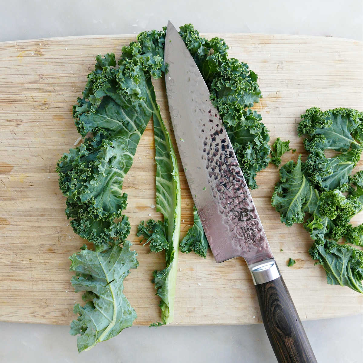 Kale being sliced on a cutting board and prepared for making chips.