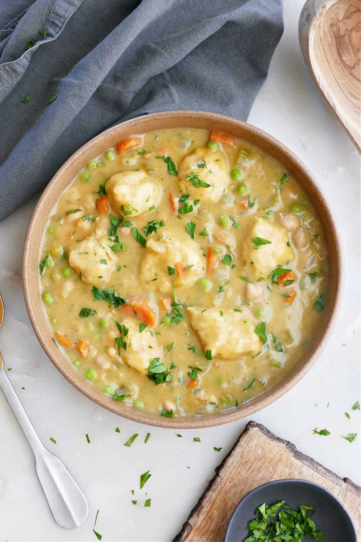 Vegan chicken and dumplings soup in a bowl next to a napkin, spoon, and garnishes.