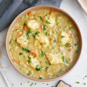 Vegan chicken and dumplings soup in a bowl next to a napkin, spoon, and garnishes.