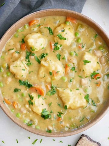 Vegan chicken and dumplings soup in a bowl next to a napkin, spoon, and garnishes.