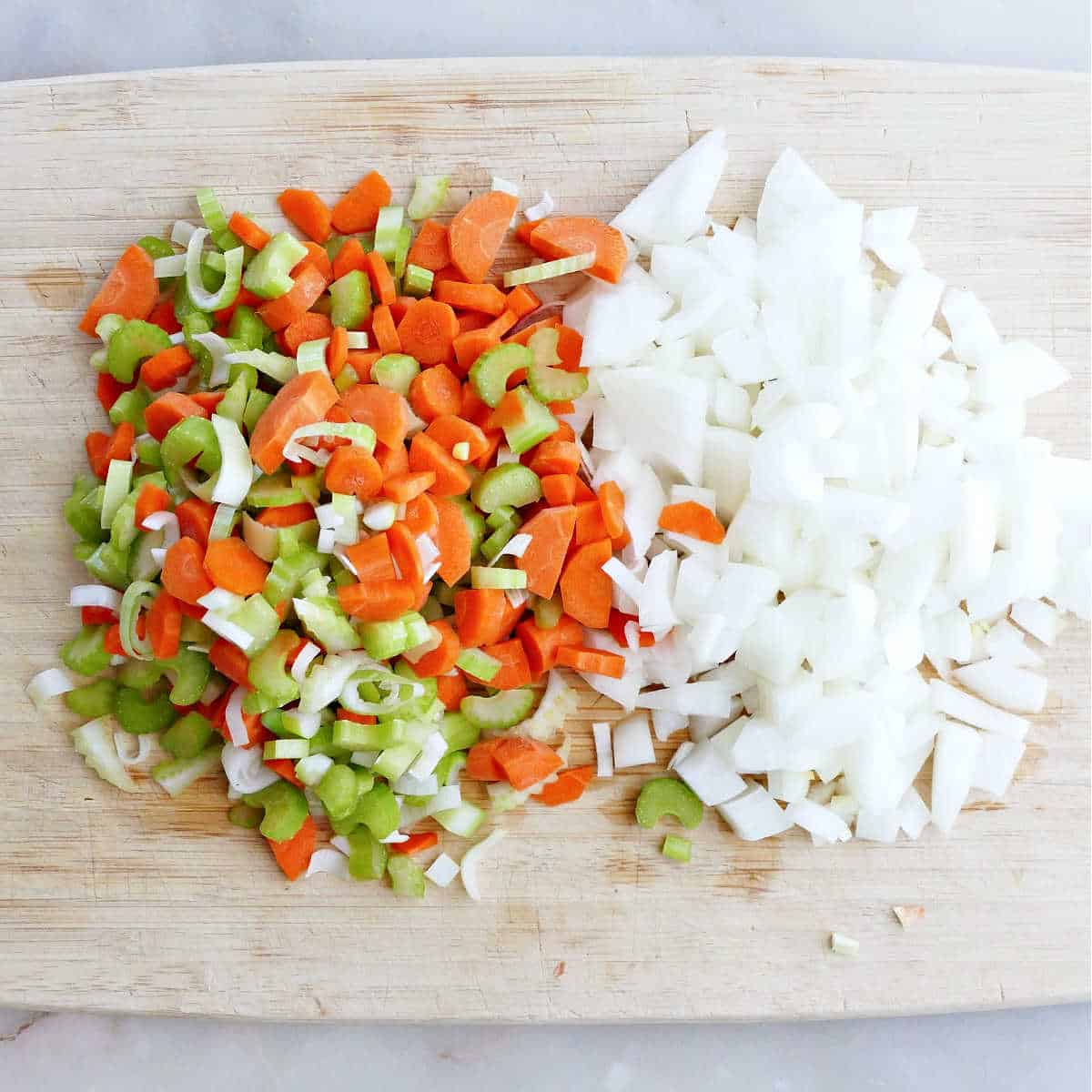 Carrots, celery, and onion diced into small pieces on a cutting board.