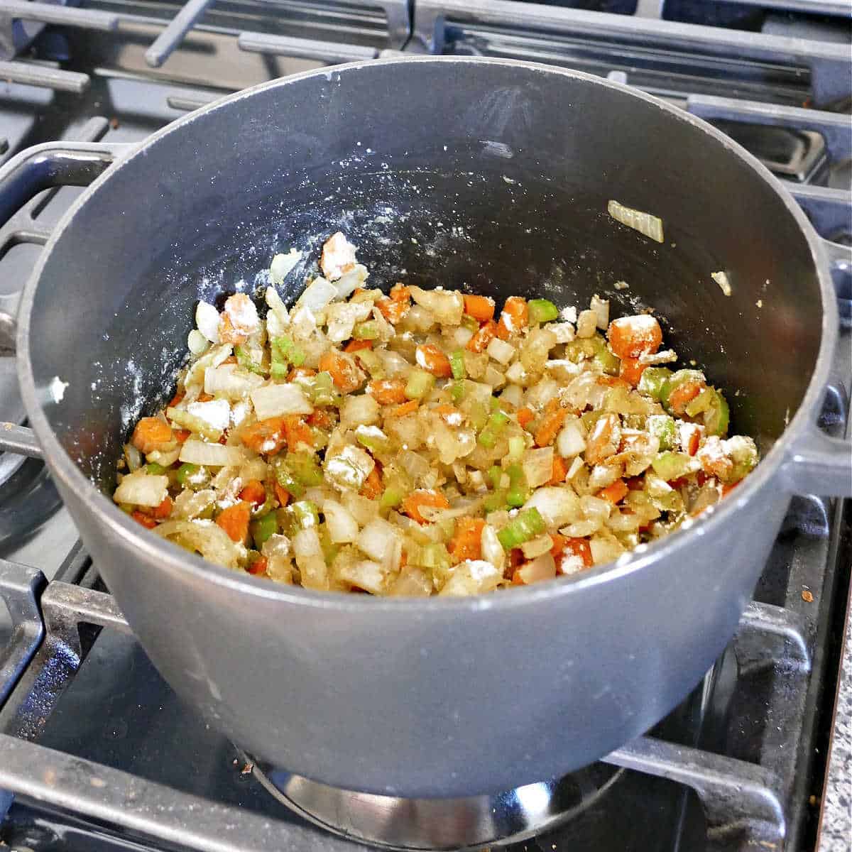 Carrots, onion, and celery coated in flour and spices cooking in a soup pot.