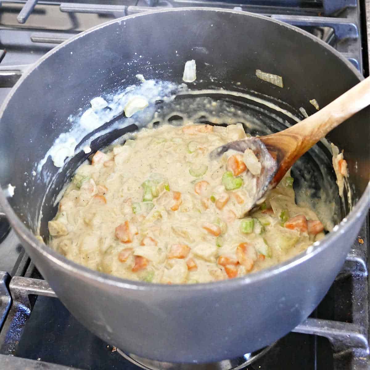 The base of vegan dumpling soup with soy milk stirred in cooking in a pot.