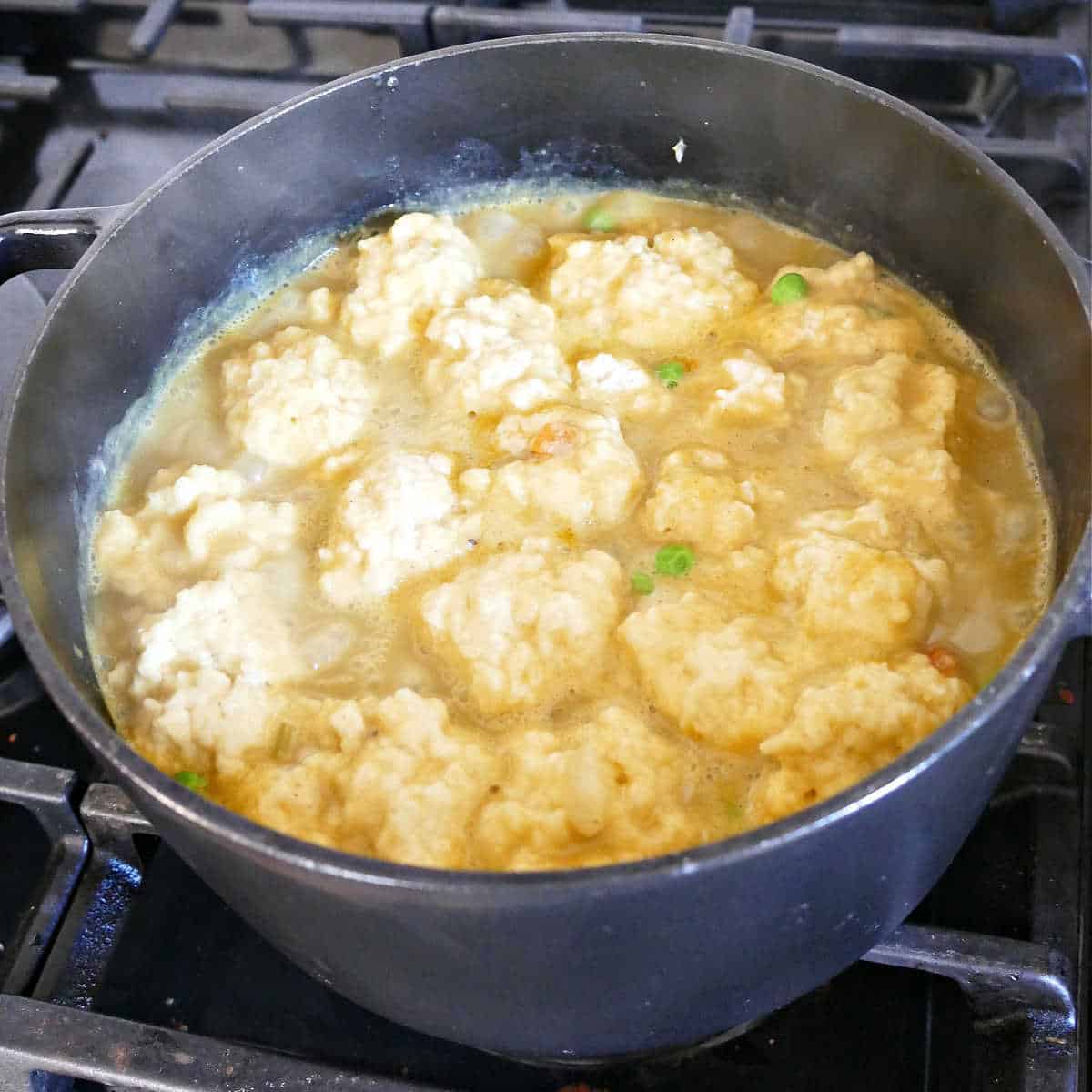 Dumplings being added to a simmering soup pot on a stove.