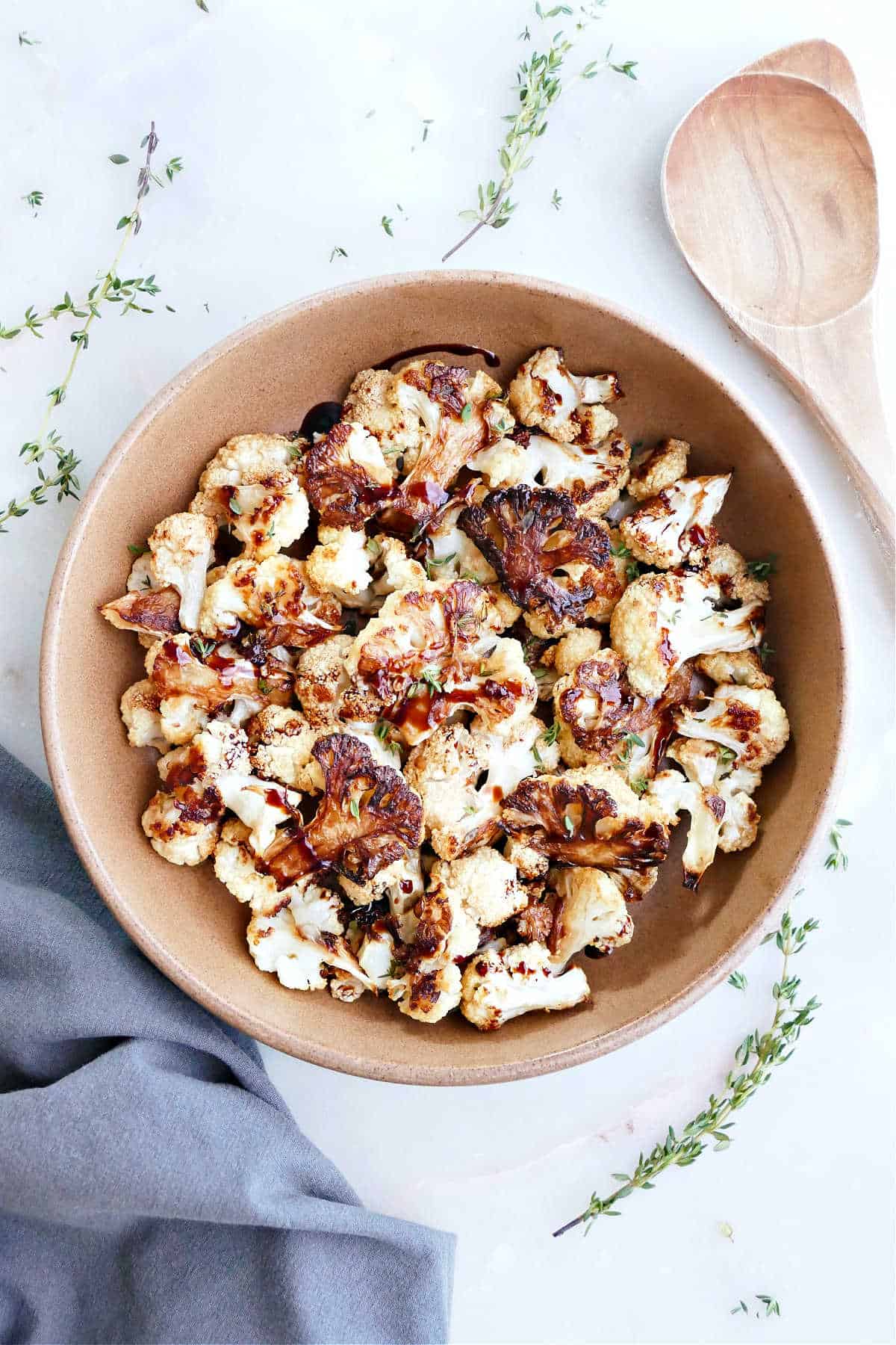 Balsamic roasted cauliflower in a bowl next to a towel and wooden spoon.