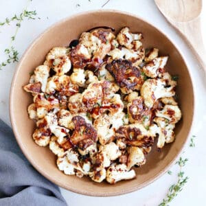 Roasted balsamic cauliflower in a large brown bowl next to a wooden spoon.