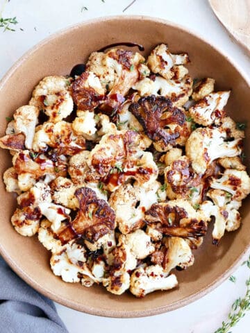 Roasted balsamic cauliflower in a large brown bowl next to a wooden spoon.