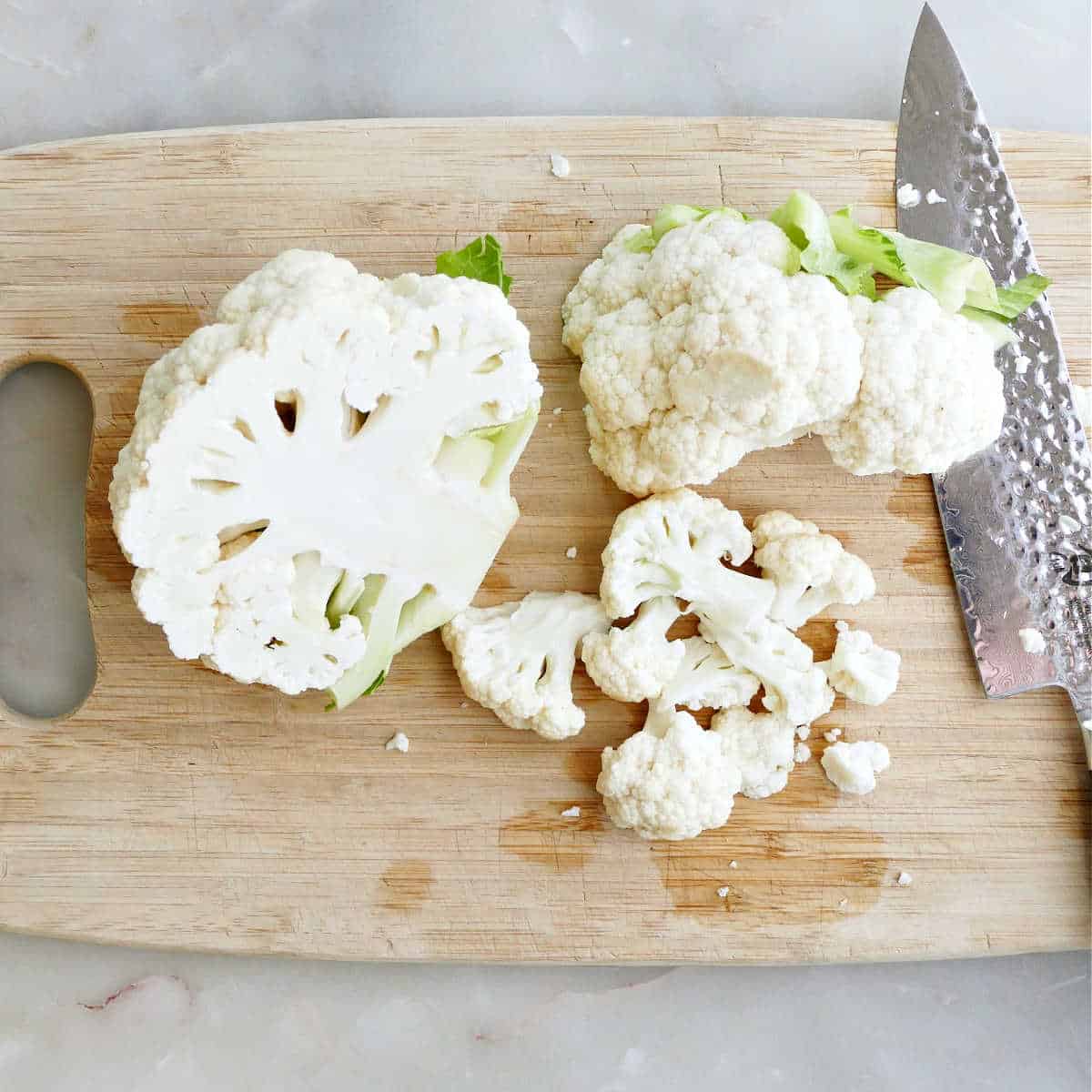 Chopped cauliflower florets on a cutting board next to a knife.