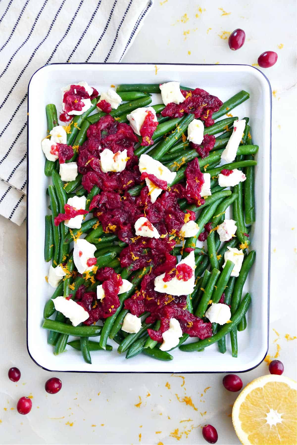 Holiday green beans in a white casserole dish topped with brie and cranberry.