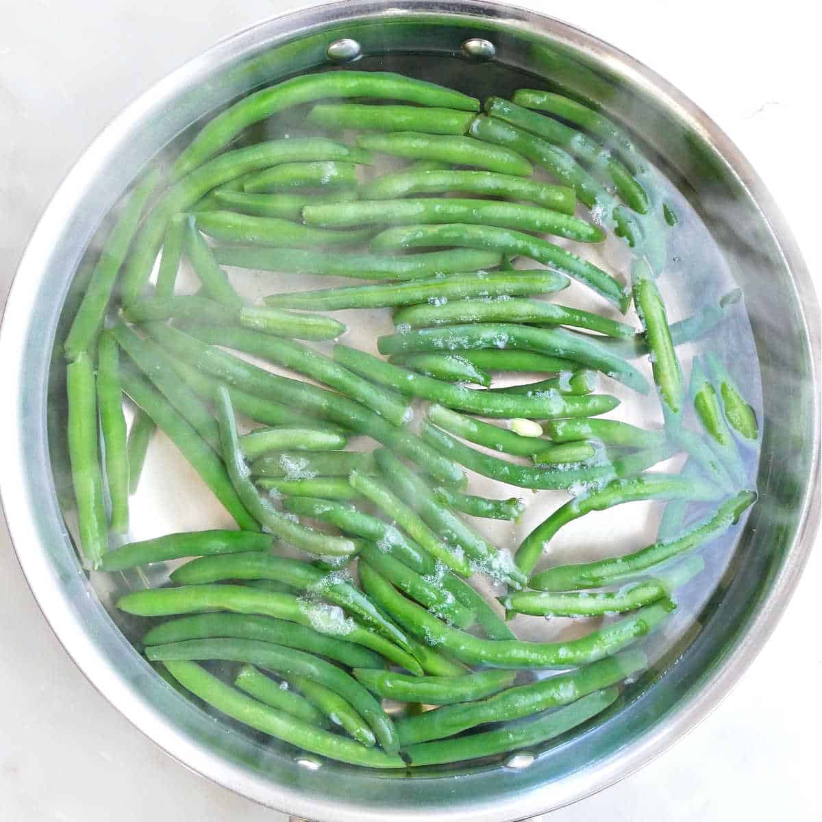 Cooking the fresh green beans in water in a large skillet.