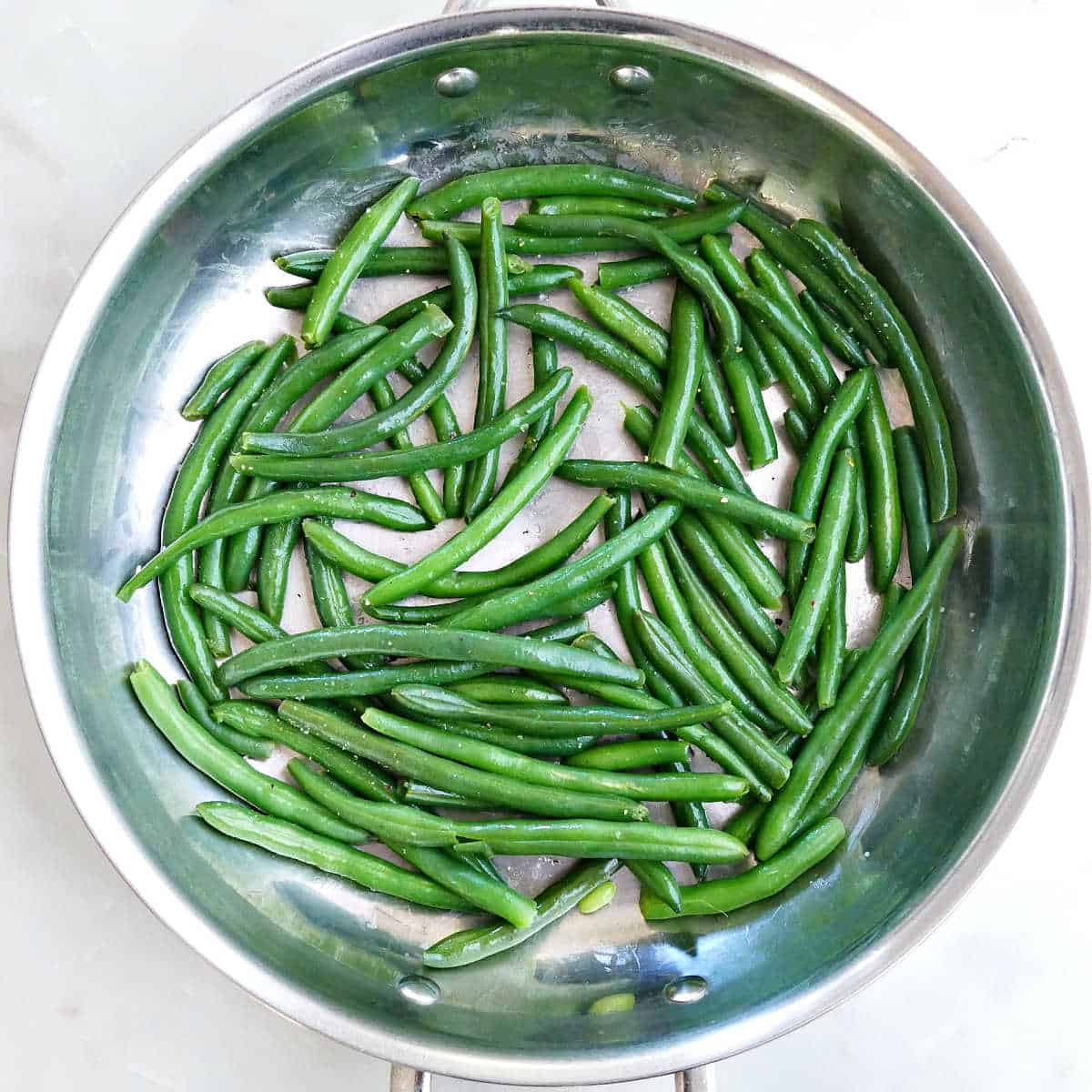 Fresh green beans that have been cooked and tossed with butter in a skillet.