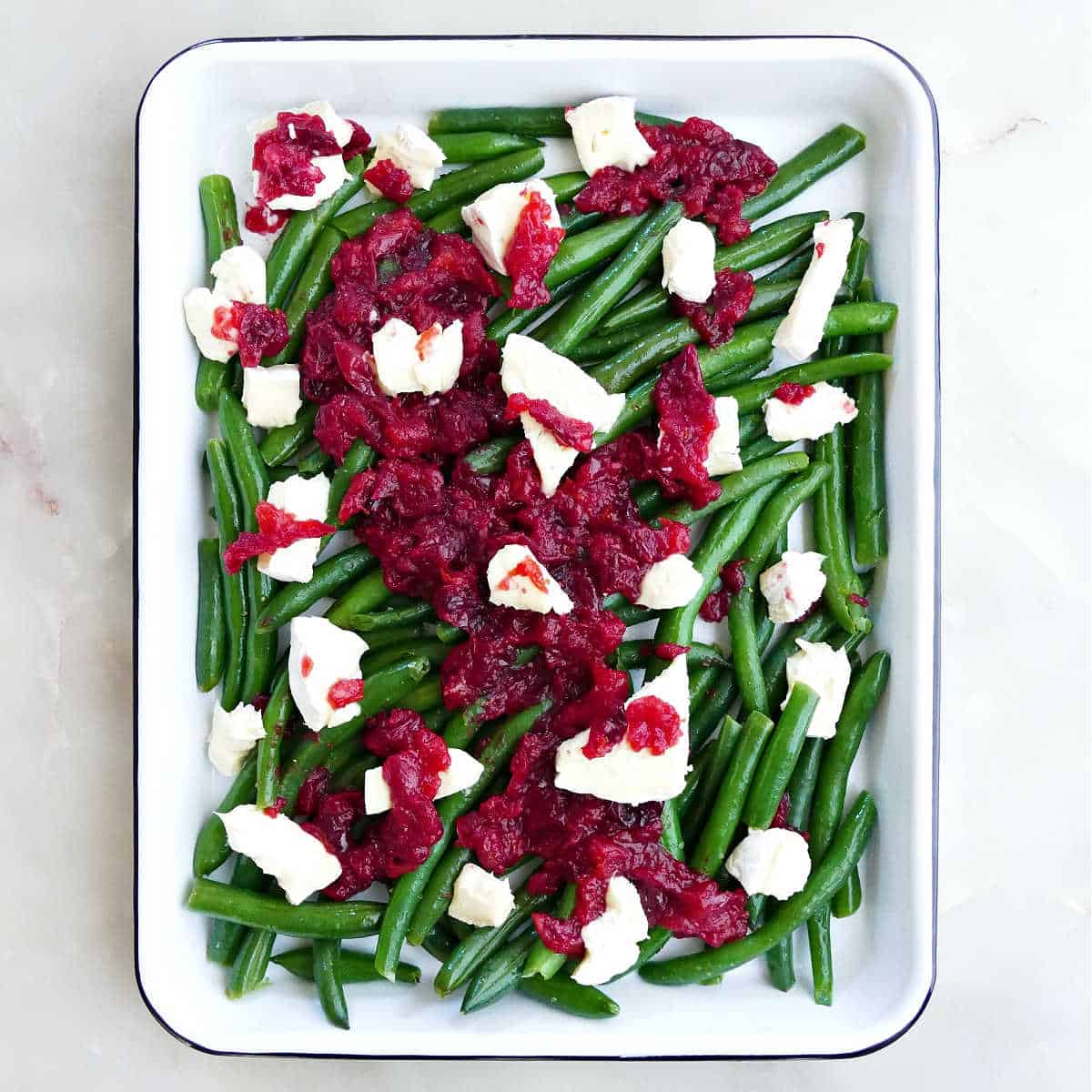 Fresh green beans in a casserole dish topped with homemade cranberry sauce and brie cheese.