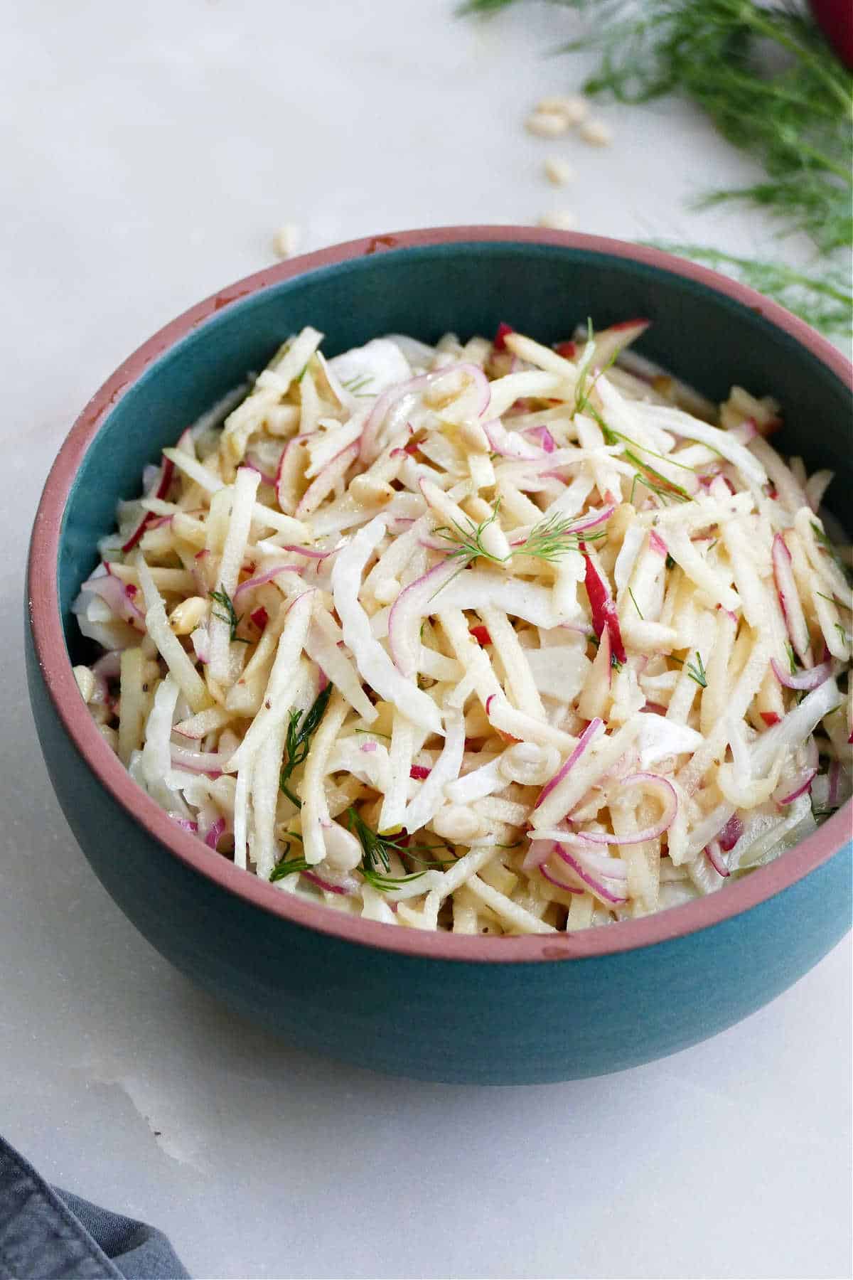 Fennel apple slaw with fresh herbs in a serving bowl on a counter.