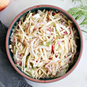 Fennel apple salad in a serving bowl next to garnishes and a napkin on a counter.