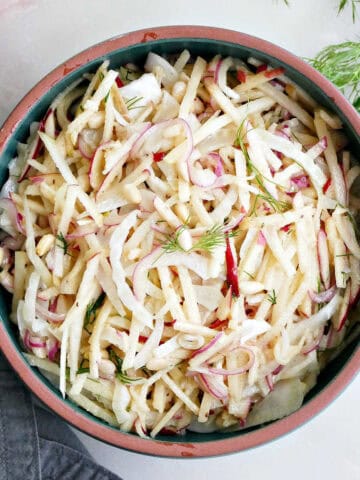 Fennel apple salad in a serving bowl next to garnishes and a napkin on a counter.