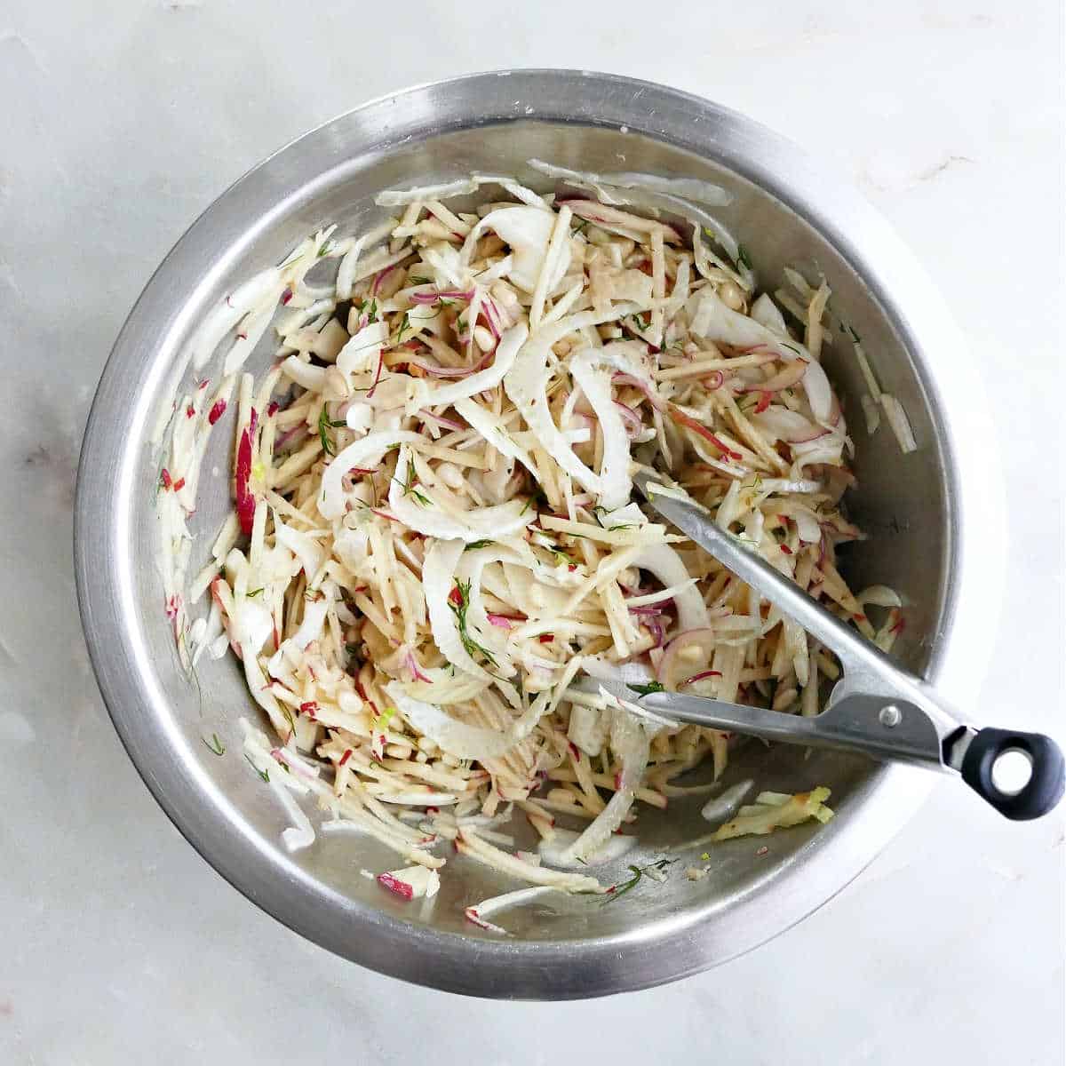 Fennel apple salad ingredients tossed with dressing in a bowl with tongs.