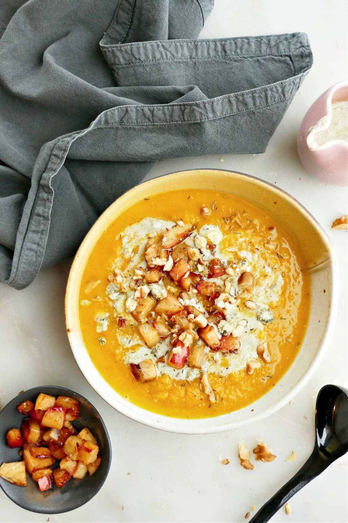 Kuri squash soup in a bowl next to a napkin, spoon, and toppings.