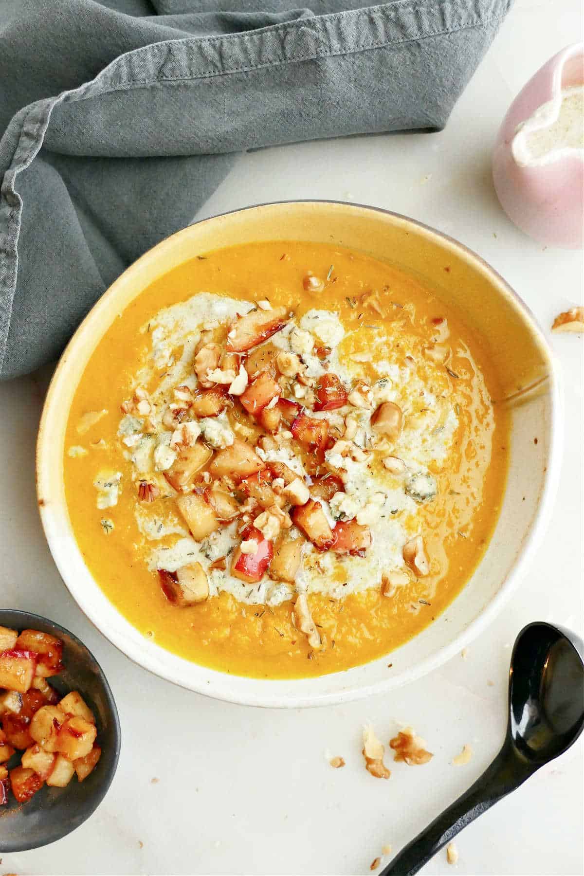 Red kuri soup with apples, walnuts, and blue cheese in a bowl.