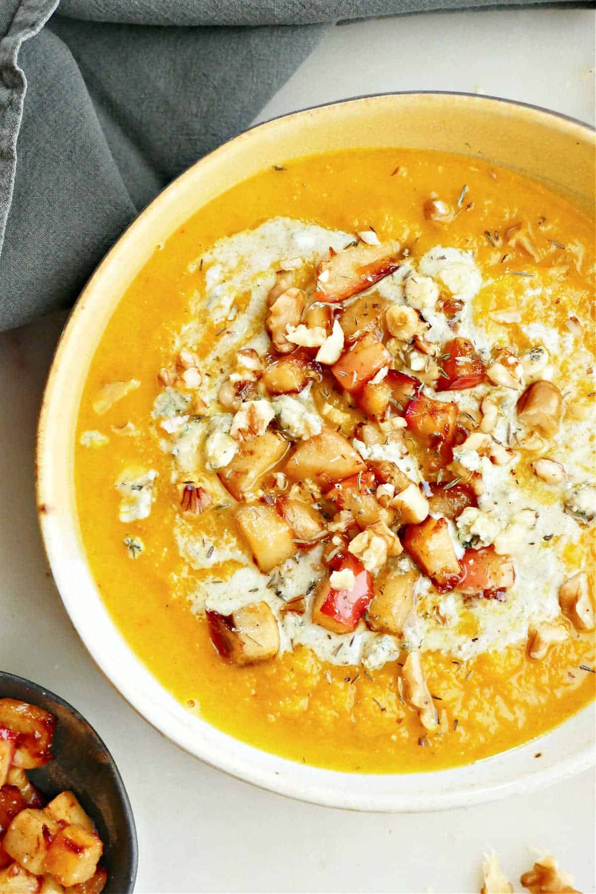 Roasted squash soup in a bowl with blue cheese drizzle, apples, and walnuts.