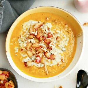 Red kuri soup with apples, walnuts, and blue cheese in a bowl.