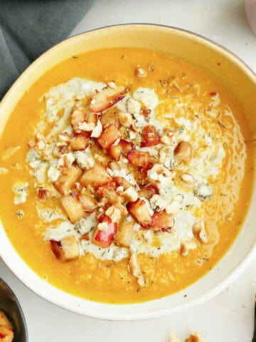 Red kuri soup with apples, walnuts, and blue cheese in a bowl.