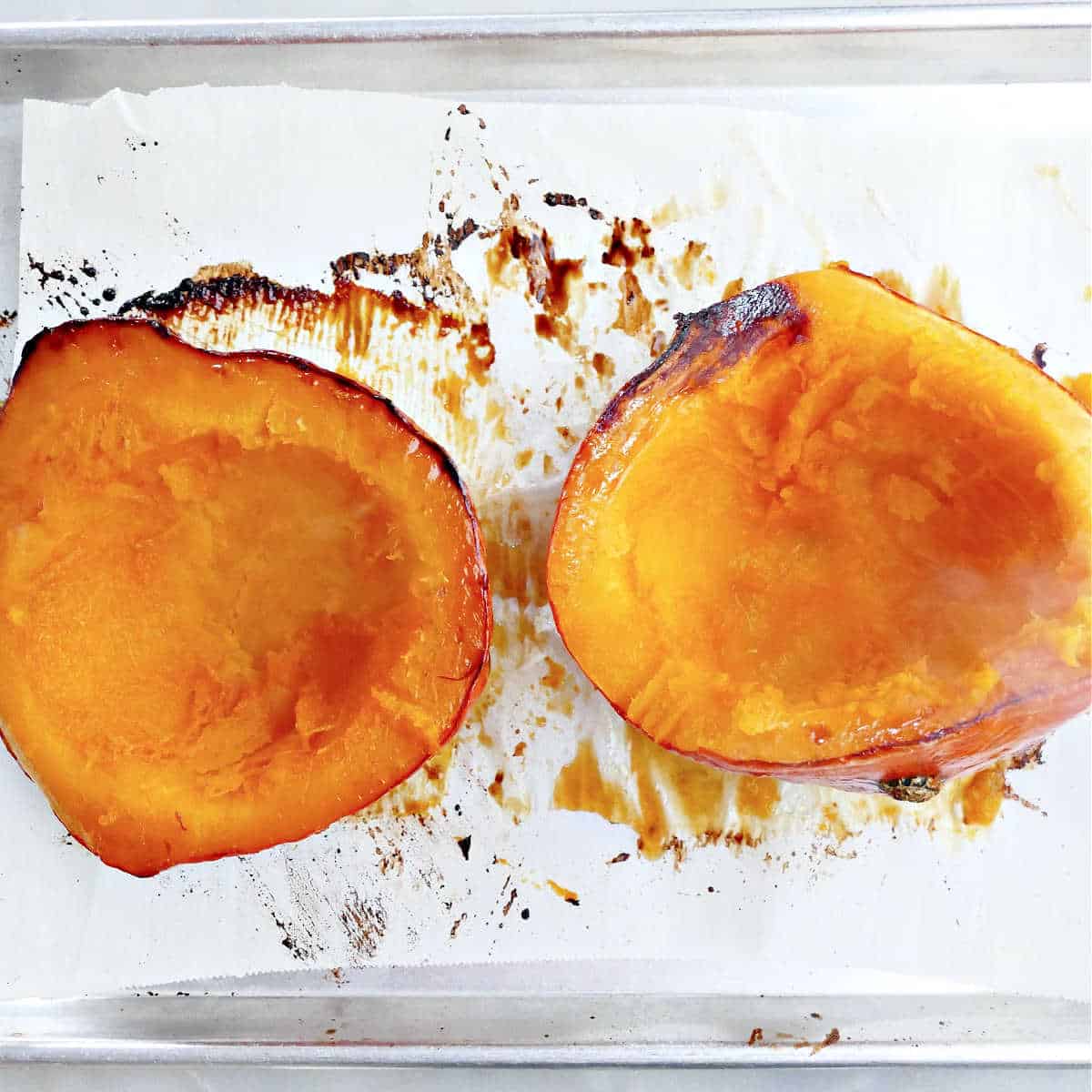 Kuri squash halves on a baking sheet after roasting in the oven.