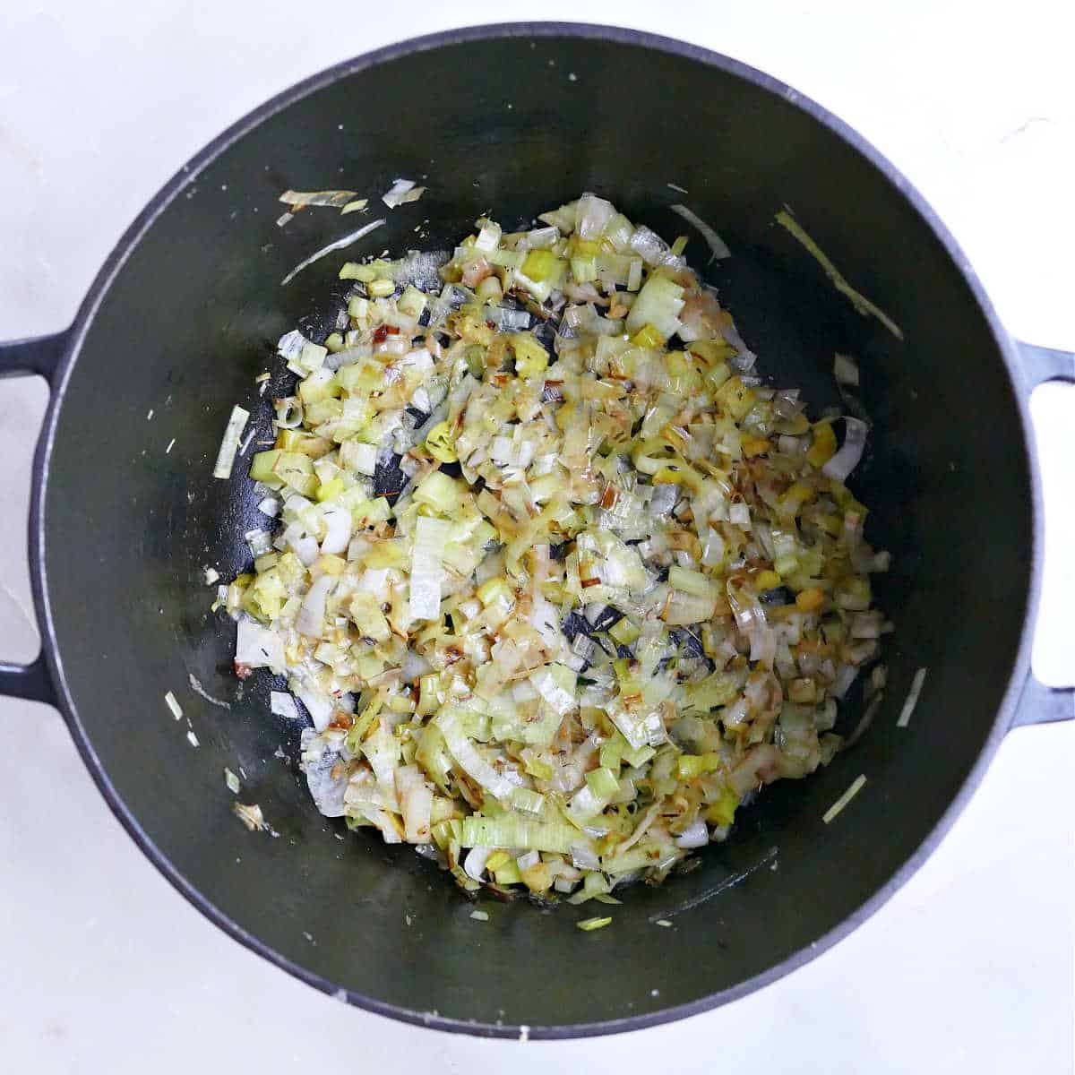 Leeks, garlic, and spices cooking in olive oil in a large pot.