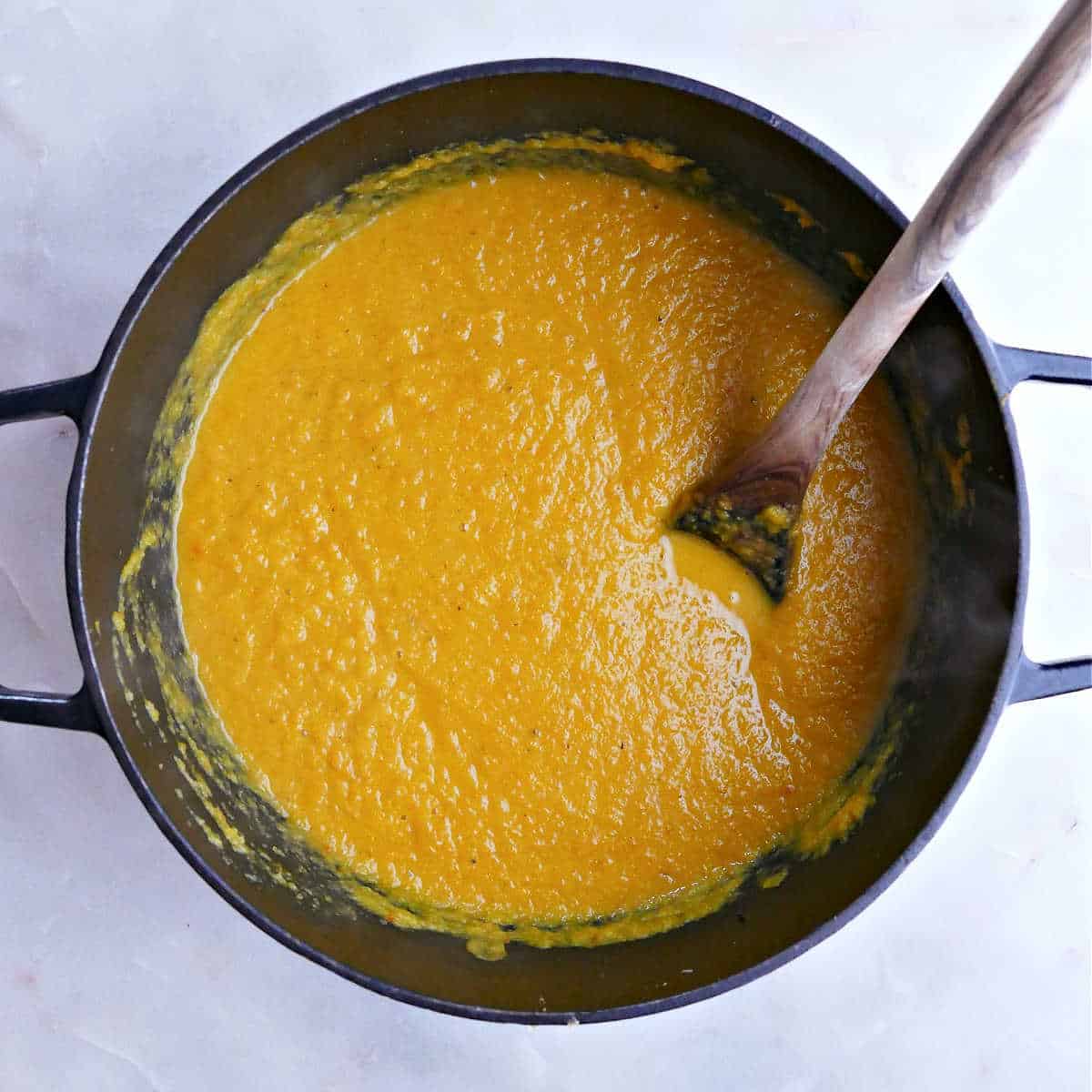 Blended kuri squash soup in large pot with a wooden spoon.