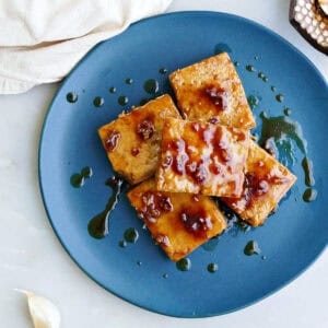 Maple glazed tofu on a blue plate stacked on top of each other with extra drizzled glaze.