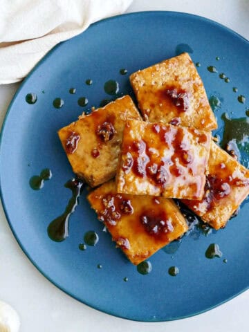 Maple glazed tofu on a blue plate stacked on top of each other with extra drizzled glaze.