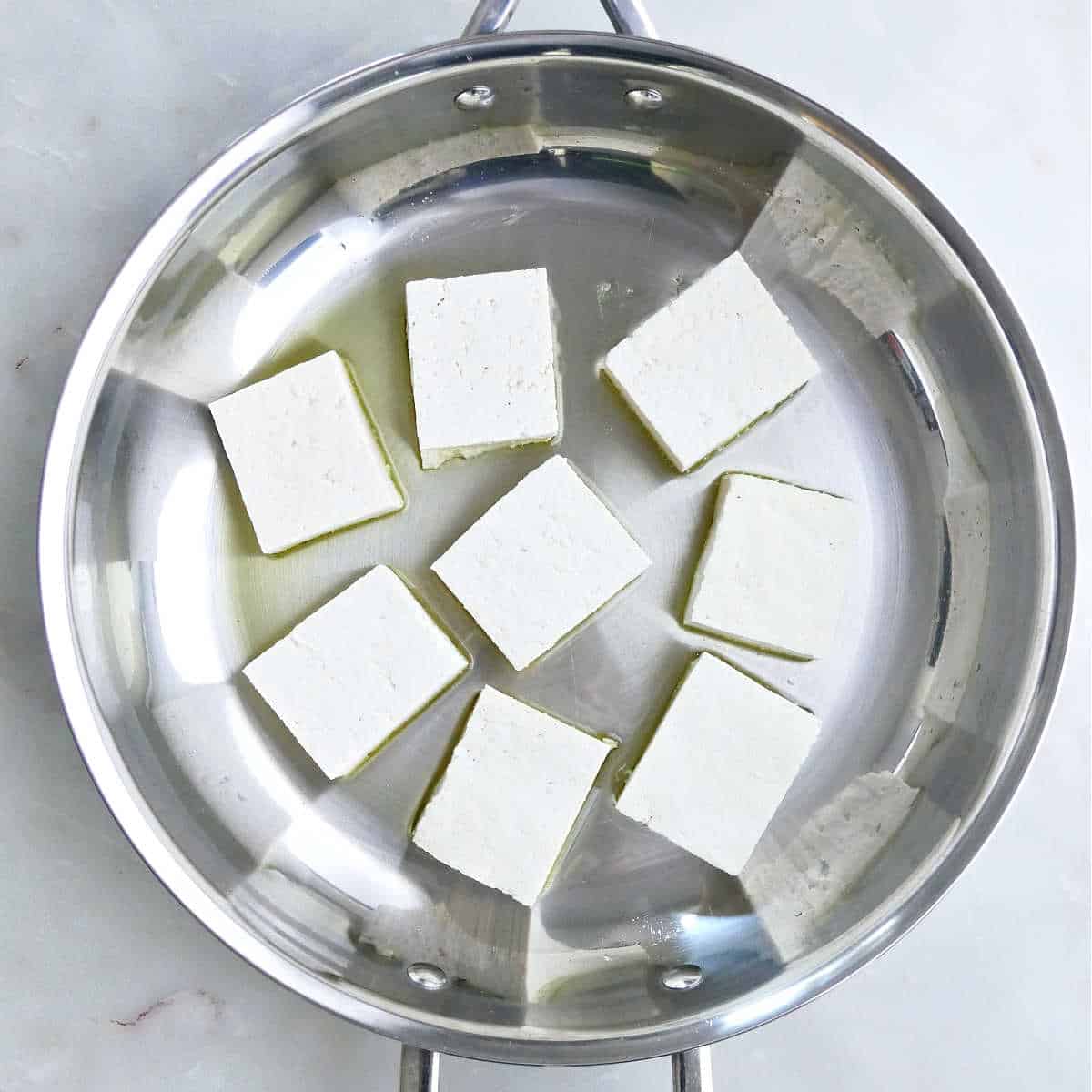 Tofu in a pan with cooking oil.