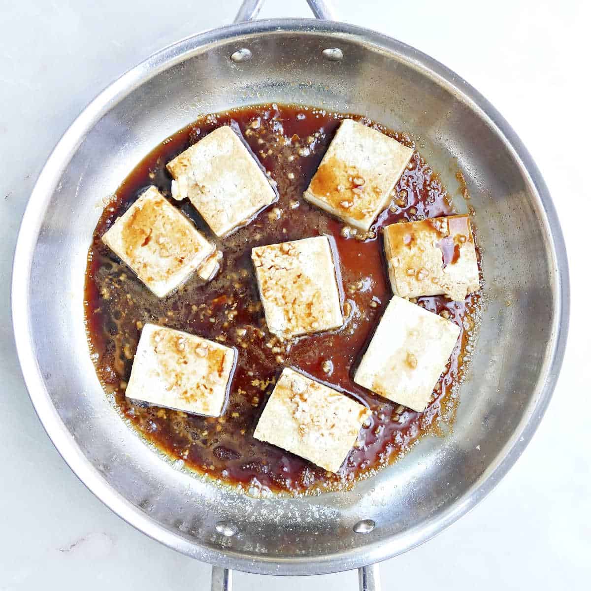 Tofu cooking in a skillet in a homemade maple glaze.